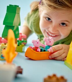 Hymyilevä lapsi leikkii Peppa Pig- ja George-hahmojen kanssa oranssissa leluveneessä.