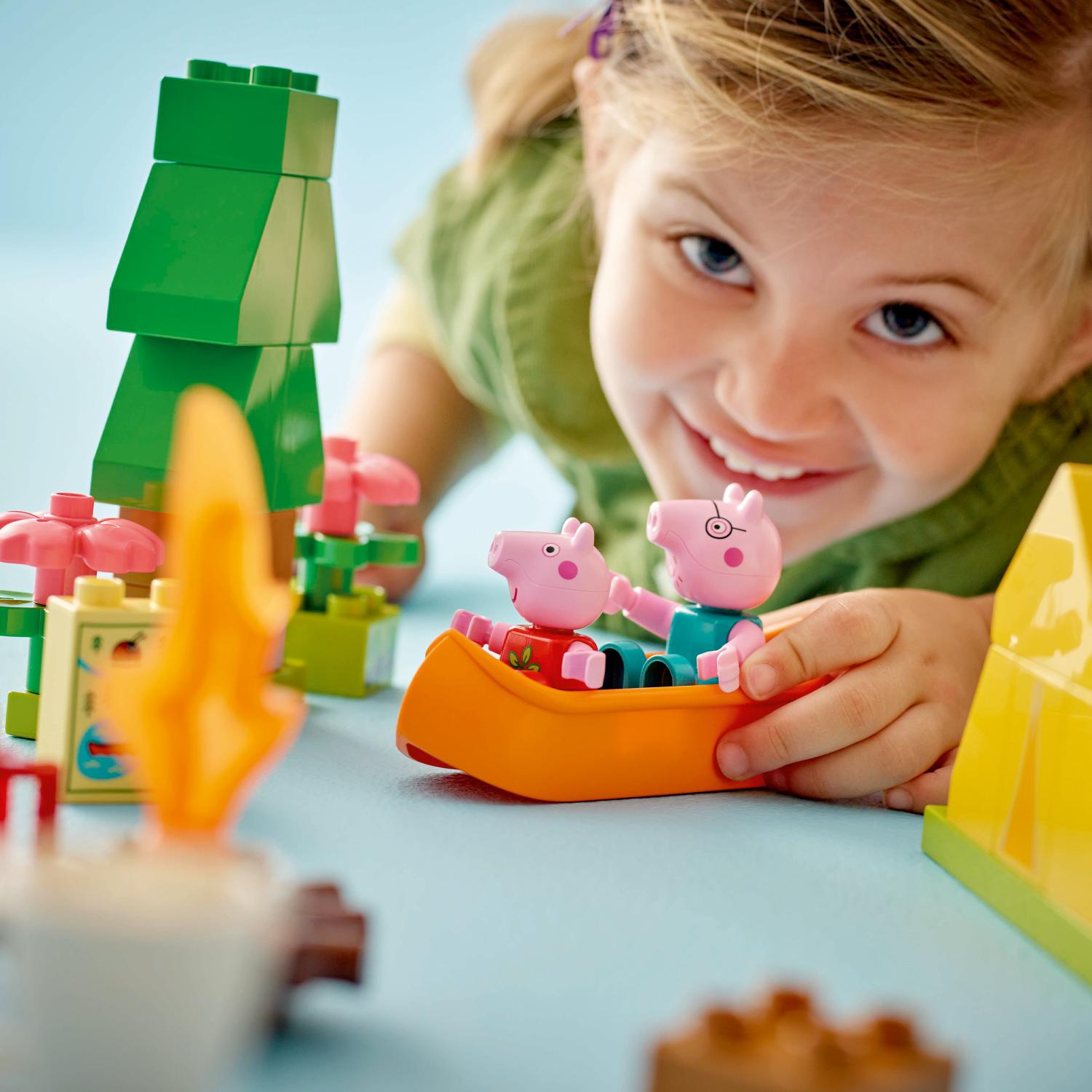 Hymyilevä lapsi leikkii Peppa Pig- ja George-hahmojen kanssa oranssissa leluveneessä.