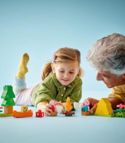 Nuori tyttö ja aikuinen mies leikkivät yhdessä Peppa Pig -aiheisilla LEGO Duplo -palikoilla vaaleansinisellä alustalla.
