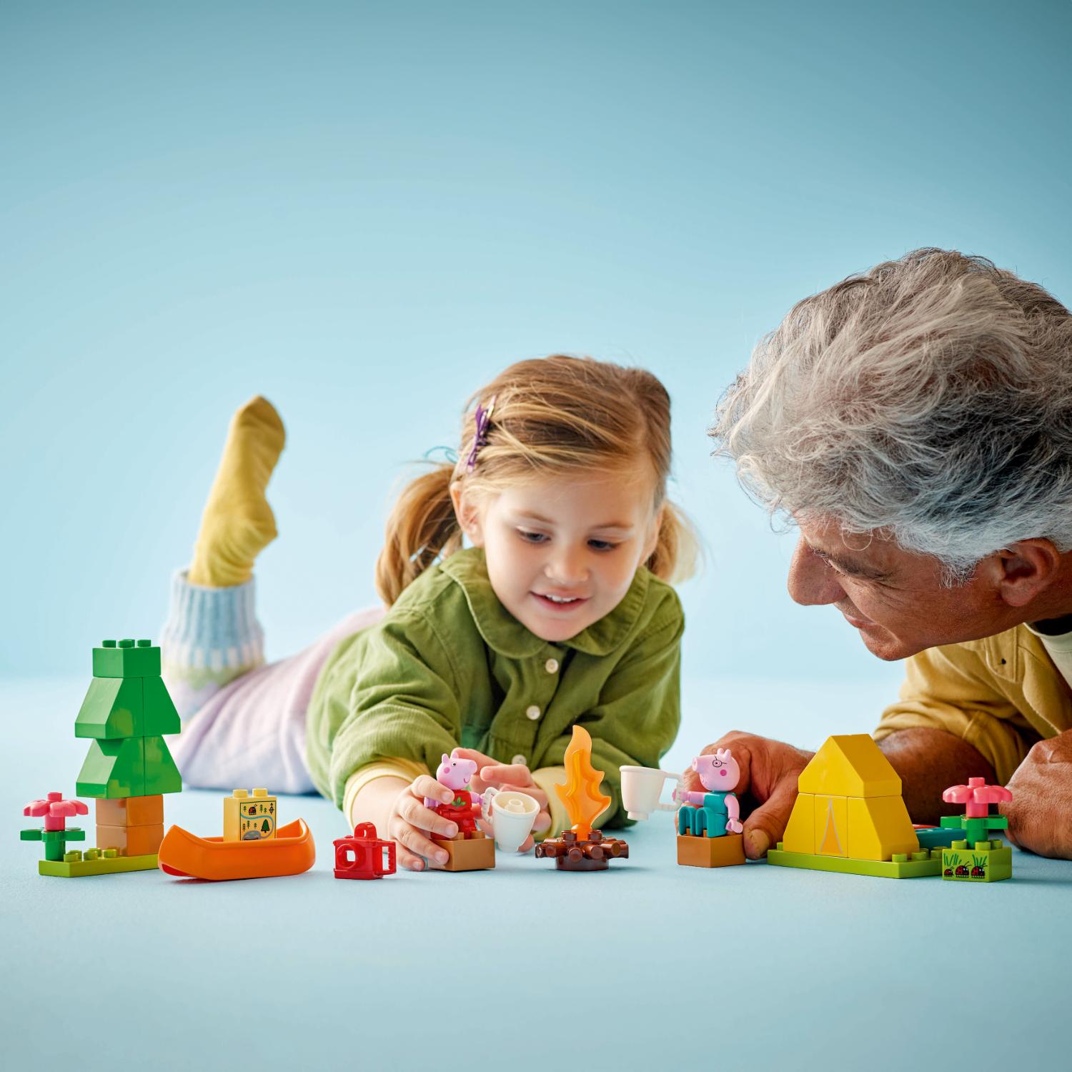 Nuori tyttö ja aikuinen mies leikkivät yhdessä Peppa Pig -aiheisilla LEGO Duplo -palikoilla vaaleansinisellä alustalla.