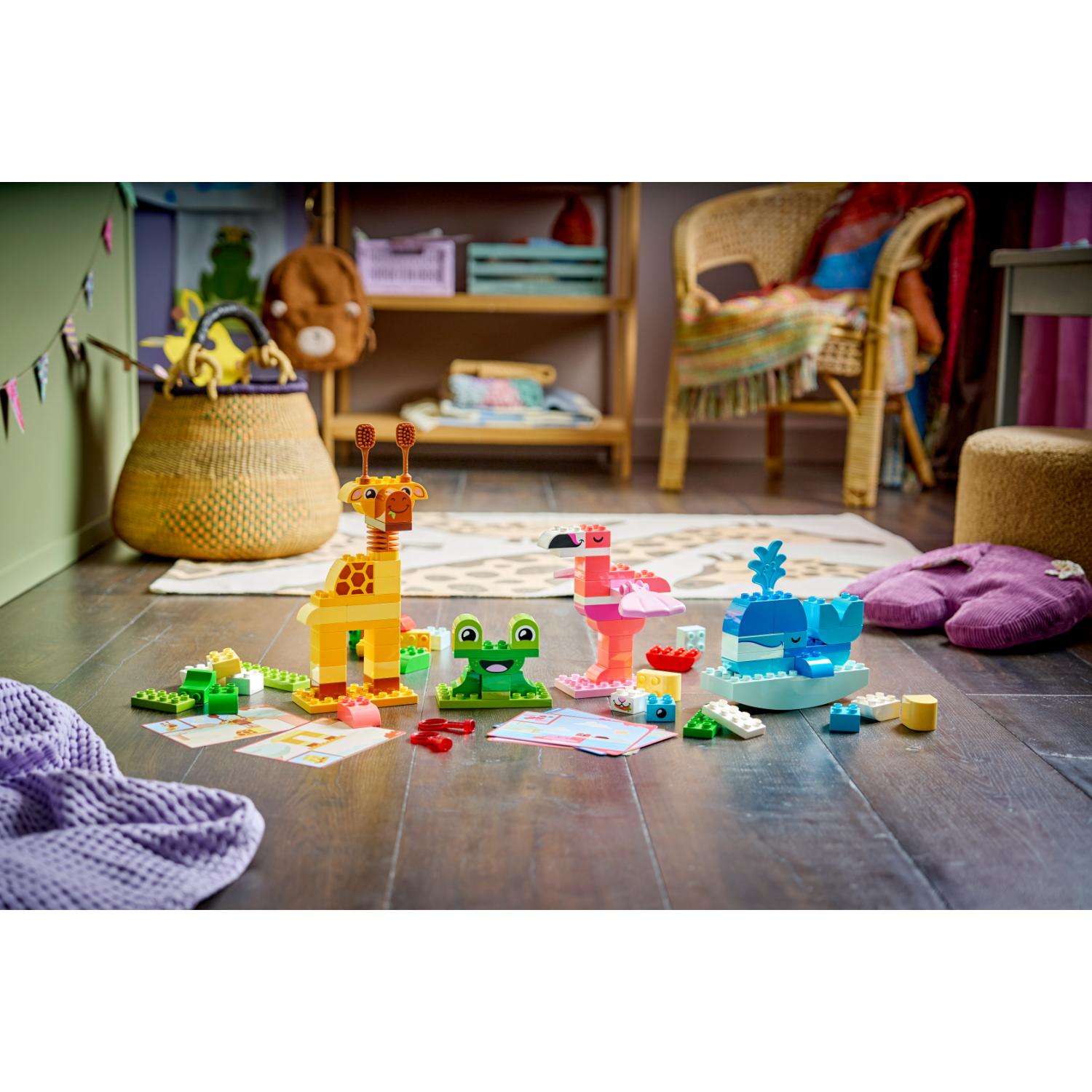 LEGO DUPLO -eläinhahmot, mukaan lukien kirahvi, sammakko, flamingo ja valas, on aseteltu puulattialle.