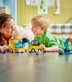 Nainen ja pieni poika leikkivät yhdessä lattialla keltaisilla LEGO-rakennusajoneuvoilla ja -hahmoilla.