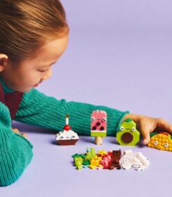 Lapsi ojentaa kätensä LEGO-tacoa kohti, ja hänen edessään on rivi muita ruoan muotoisia LEGO-luomuksia, kuten cupcake, jäätelöpuikko ja avokado.