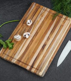 Tumman työtason päällä on Leikkuulauta lucy tiikkiä -niminen 45 x 30 cm:n kokoinen raidallinen puinen leikkuulauta, jonka päällä on kolme viipaloitua sieniä, selleriä, tuoretta tilliä ja kokkiveitsi.