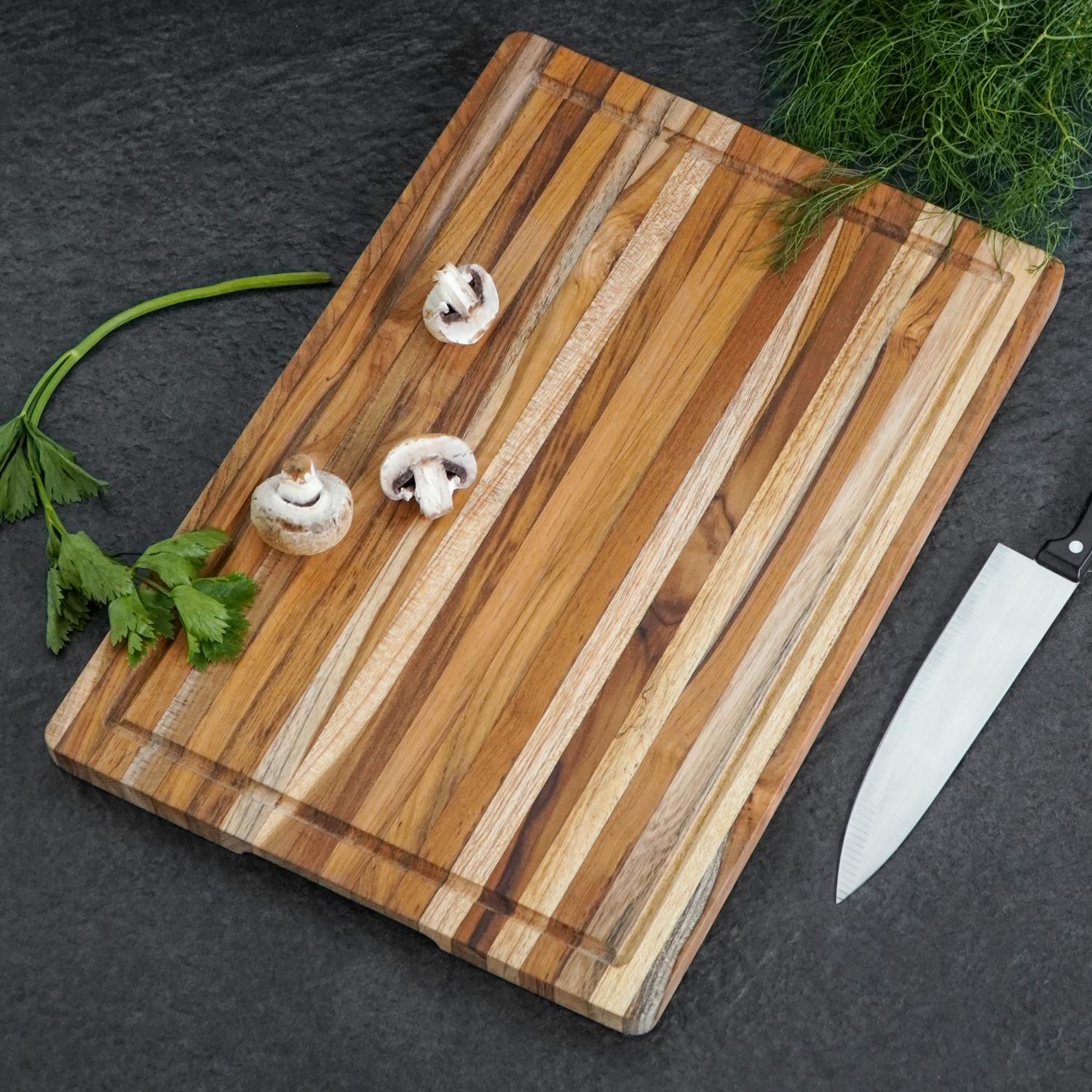 Tumman työtason päällä on Leikkuulauta lucy tiikkiä -niminen 45 x 30 cm:n kokoinen raidallinen puinen leikkuulauta, jonka päällä on kolme viipaloitua sieniä, selleriä, tuoretta tilliä ja kokkiveitsi.