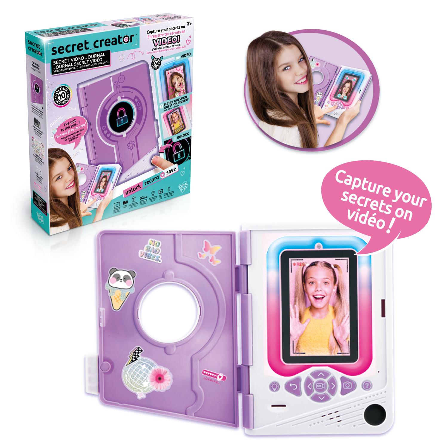 Violetti Secret Creator -videopäiväkirja-lelu, sen pakkaus sekä tyttö, joka hymyilee käyttäessään sitä. Päiväkirjassa on näyttö, jolla näkyy tytön kasvot ja tarroja, sekä teksti: ”Tallenna salaisuutesi videolle!”.