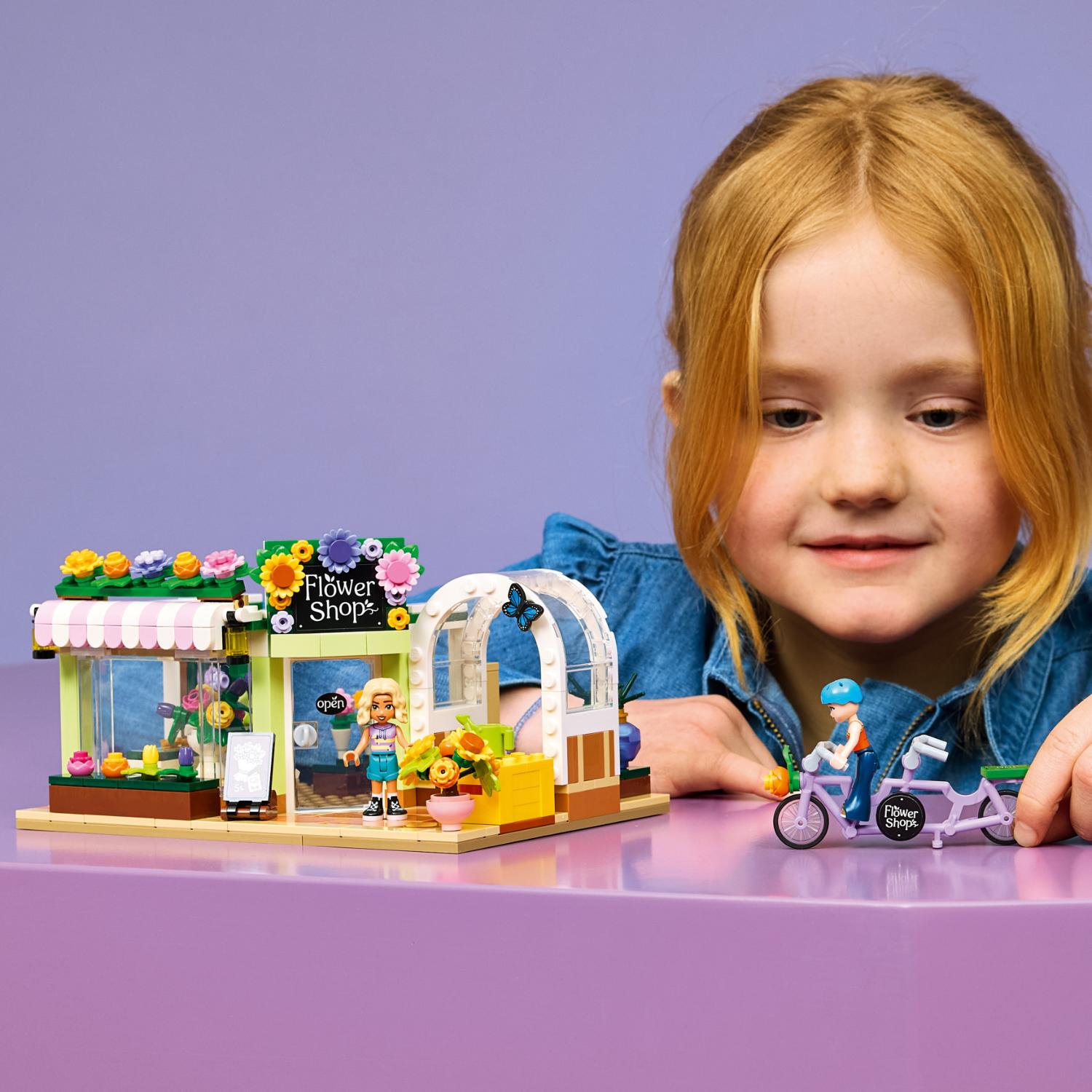Lapsi rakentaa LEGO Friends -sarjan kukkakauppasetin, johon kuuluu myymälän julkisivu, minihahmo ja polkupyörä.