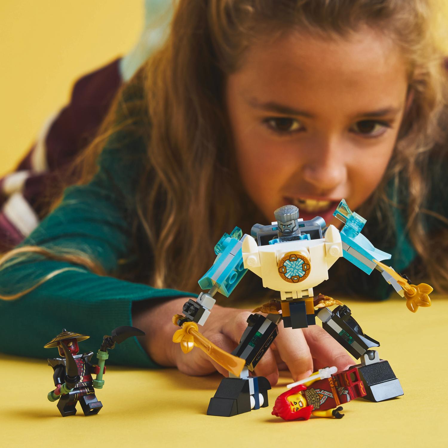 Lapsi leikkii kolmella Ninjago-Lego-hahmolla, joihin kuuluu suuri valkoinen ja sininen robotti, pieni ninja, jolla on viikate, sekä kaatunut ninja-hahmo.