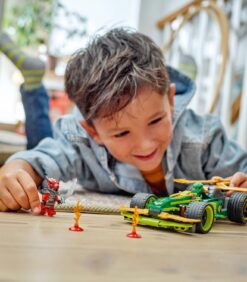 Lattialla makaa lapsi, joka leikkii vihreällä leluautolla ja punaisella LEGO-ninjahahmolla.