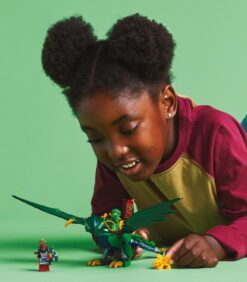 Nuori tyttö leikkii vihreällä taustalla vihreällä Lego-lohikäärmeellä, Lego-minihahmolla ja pienellä kultaisella olennolla.