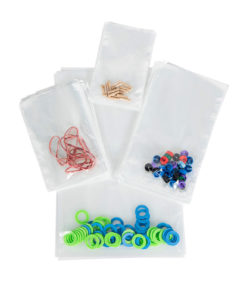 Pe-pussi, joukko kirkkaita muovipusseja, jotka on täytetty värikkäillä muovikiekoilla ja pienillä metalliesineillä, on järjestetty valkoiselle pinnalle.